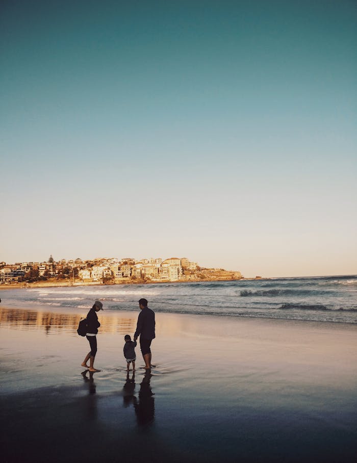 A family enjoying a peaceful walk along Bondi Beach during sunset, with city views in the background.