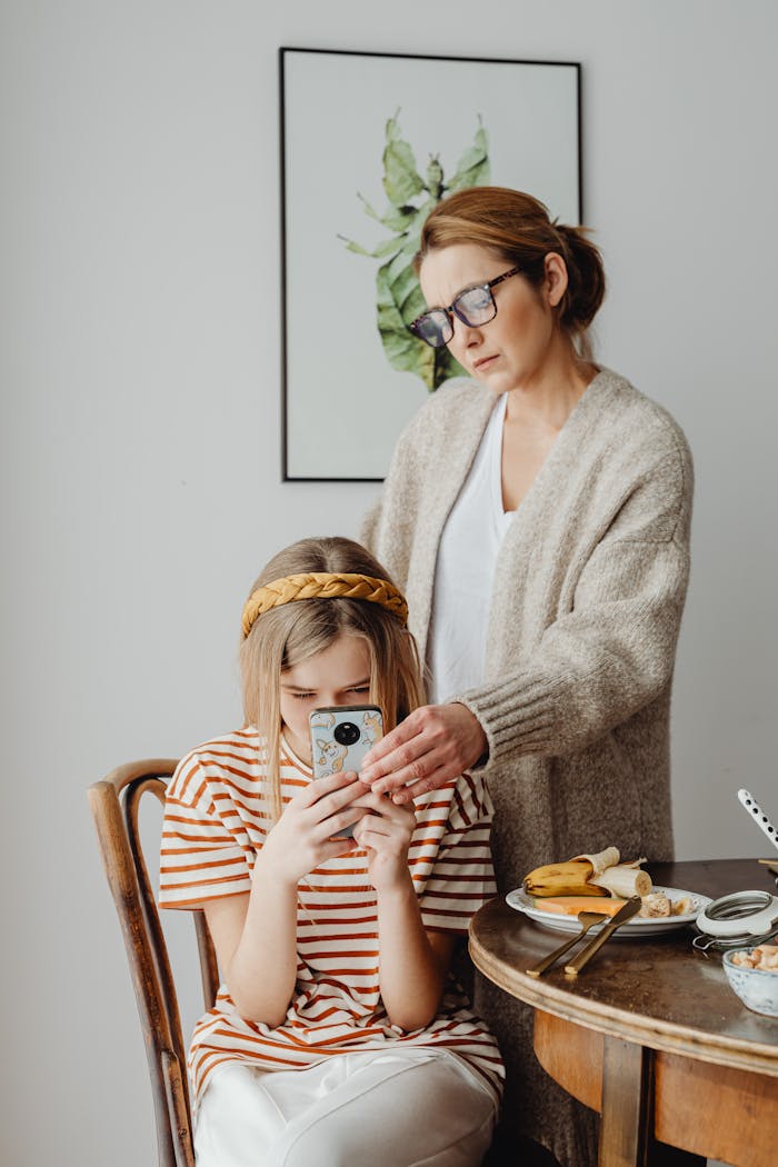 A mother and daughter at breakfast with a smartphone, expressing modern family dynamics.